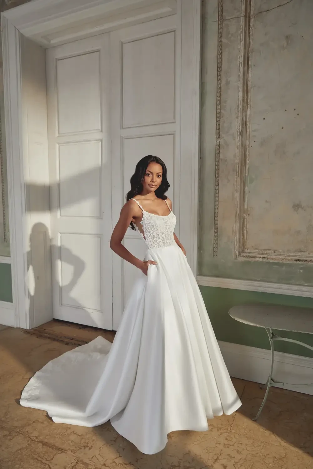 A woman wearing a white wedding dress with a fitted bodice and a flowing skirt stands in an elegant room.