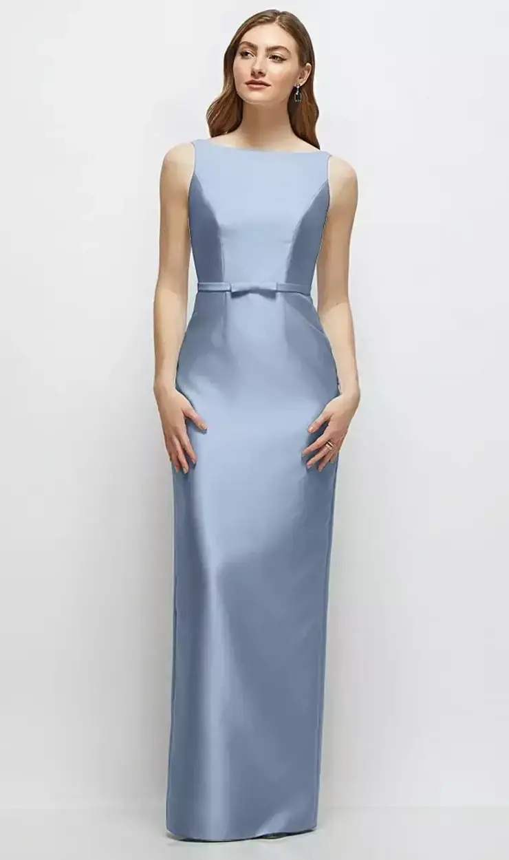A woman in a long, light blue satin dress with a fitted bodice and a bow at the waist, standing against a plain background.