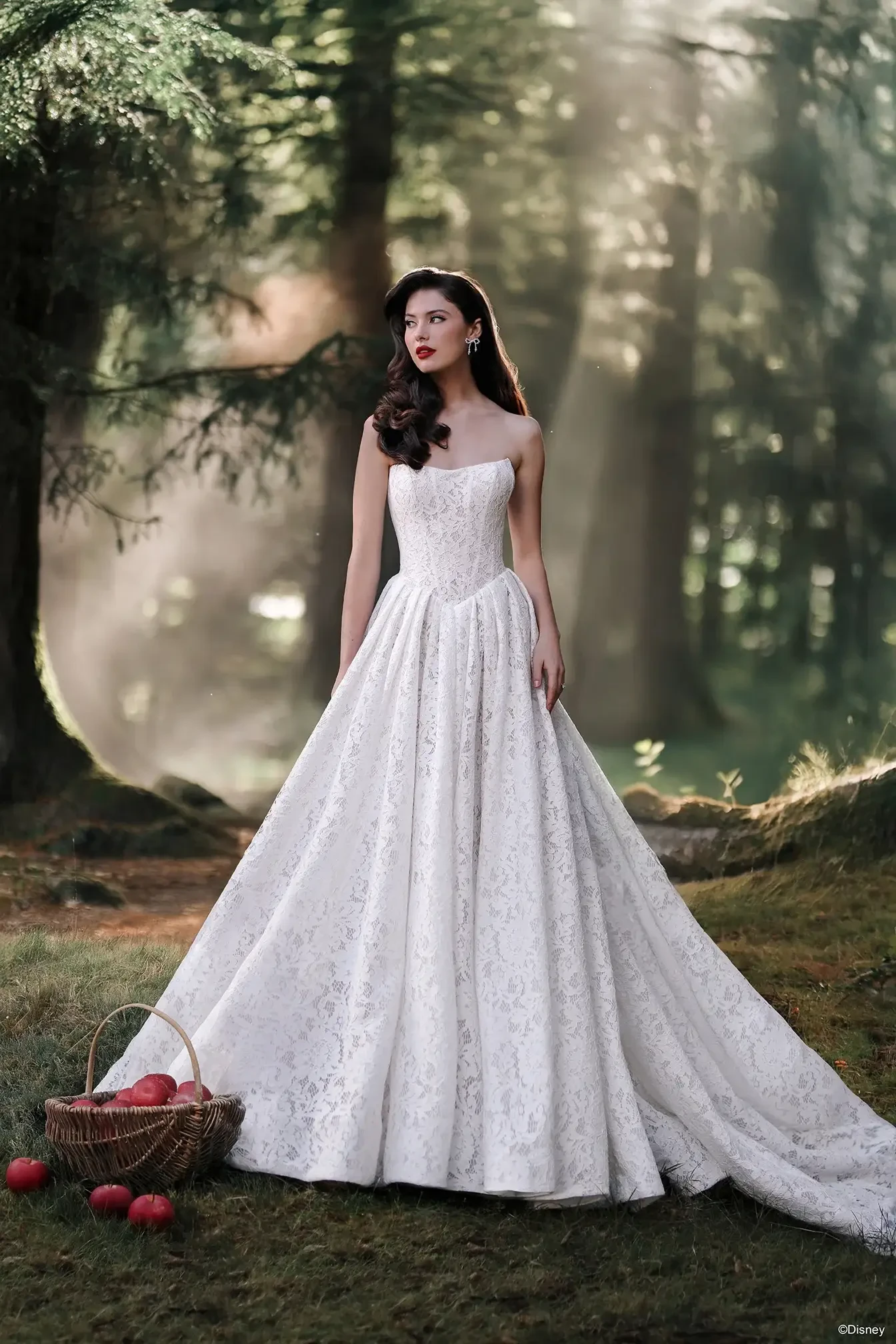A woman in a white gown standing in a forest, holding a basket of apples.