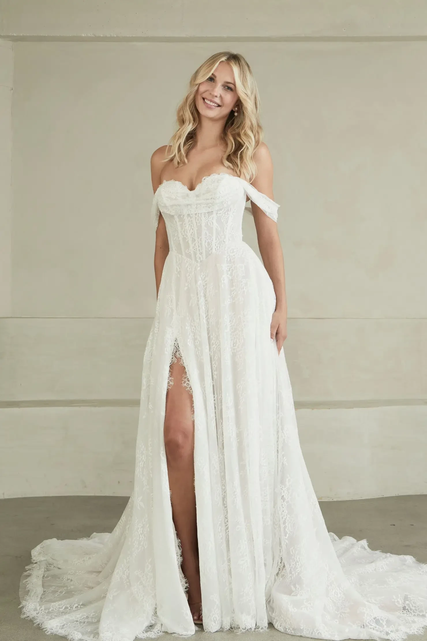 model is wearing an off the shoulder a-line wedding dress with a basque waist