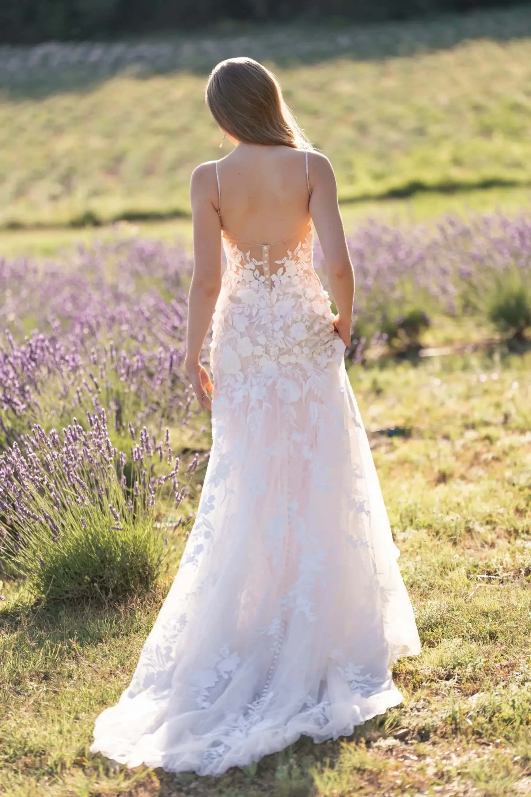 model is wearing a sleeveless sheath lace basque waist wedding dress with an open back