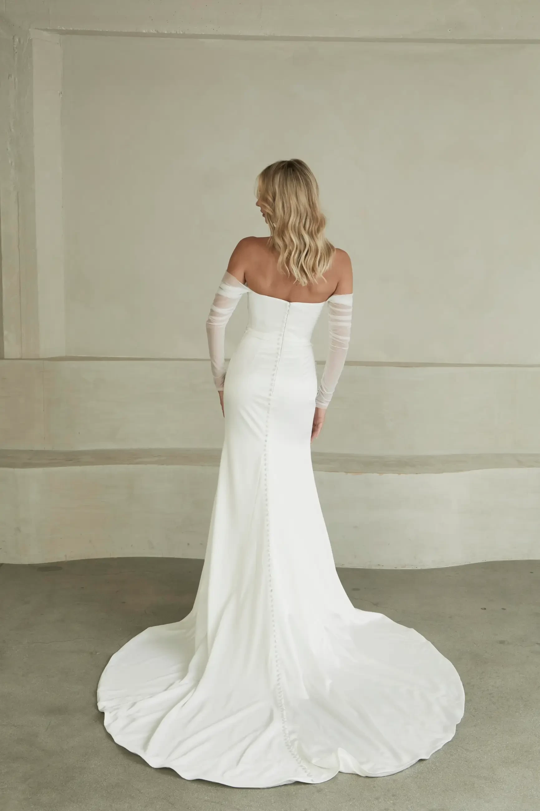 model is wearing an off the shoulder fit and flare wedding dress with sheer long sleeves