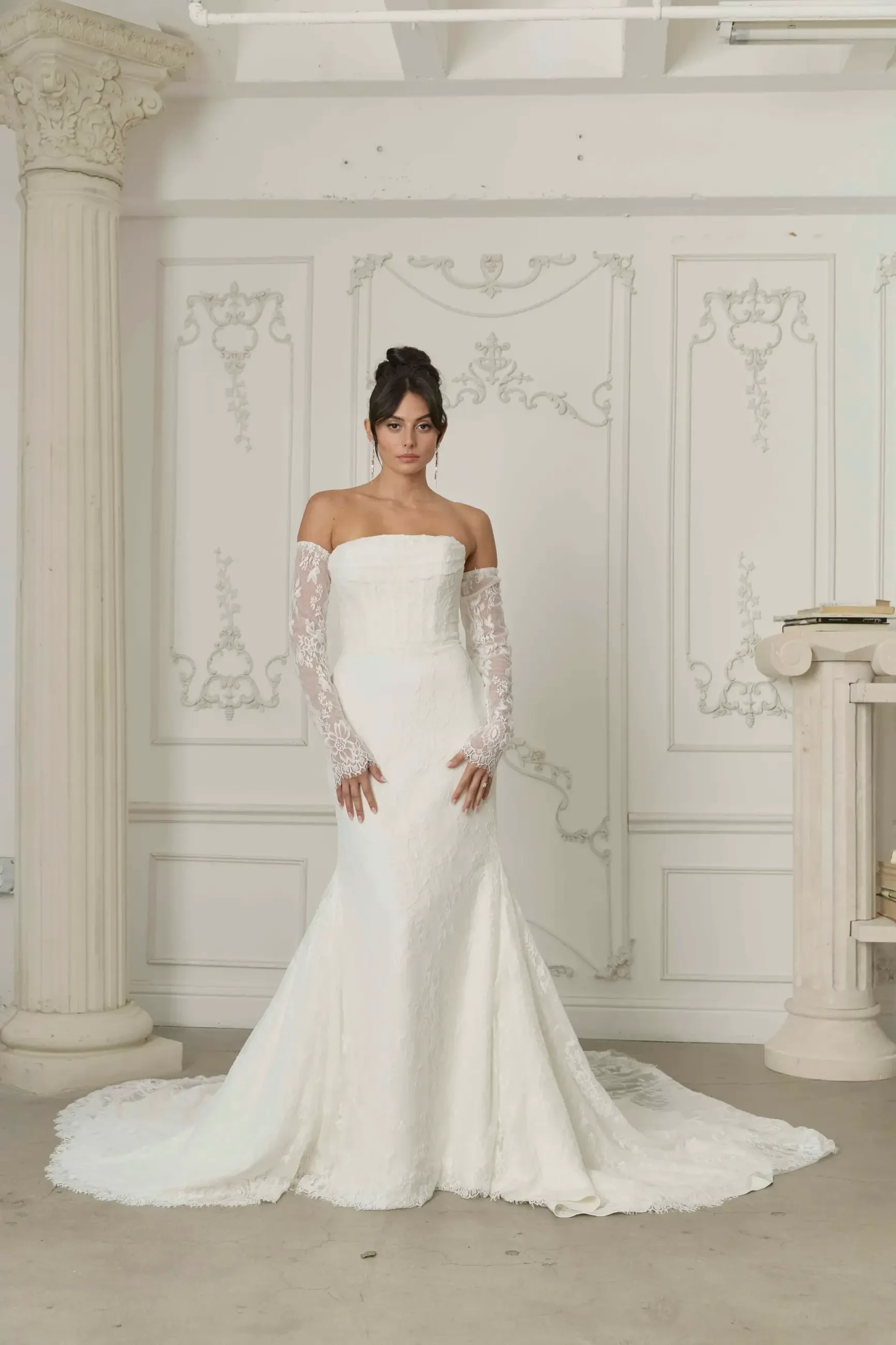 model is wearing a strapless fit and flare bridal gown with detachable long off the shoulder lace sleeves